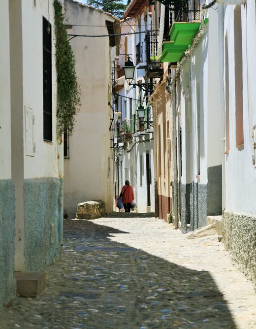A narrow cobbled lane between whitewashed houses with lanterns and plants in the Albaicín