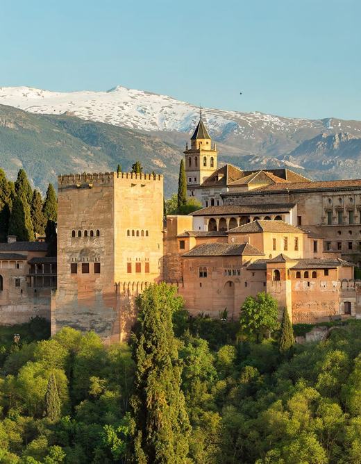 The Alhambra palaces and towers above green woods at sunset, with the snow-capped Sierra Nevada behind, seen from the Mirador de San Nicolás